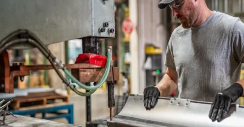 Worker forming sheet metal on an industrial machine while wearing protective gloves in a factory setting