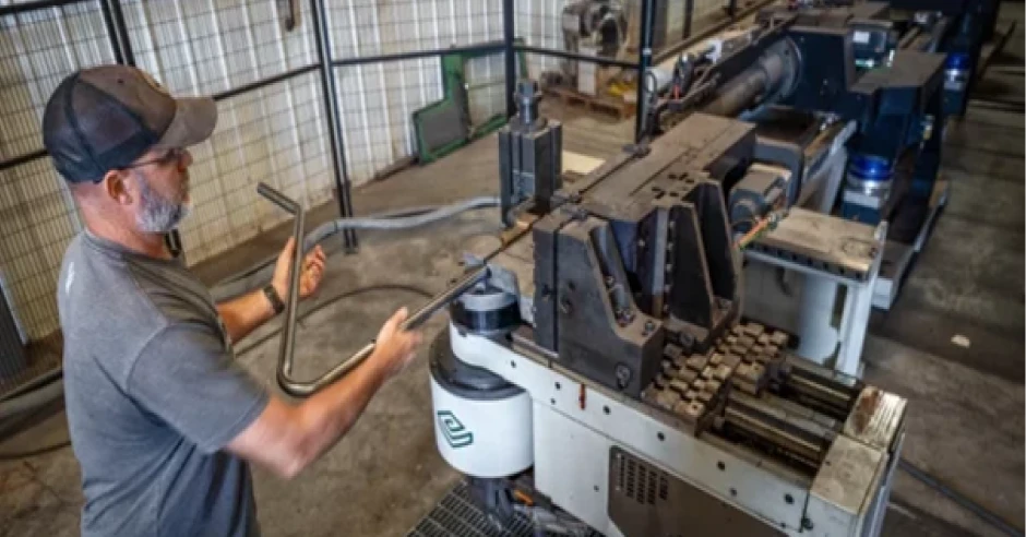 Factory worker operating a metal bending machine while shaping tubular metal components